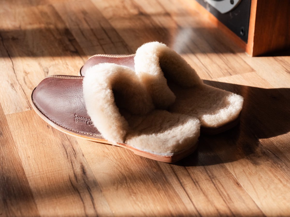 Sheepskin Slippers - Men - New Design in Dark Coffee Brown, side view of a pair in warm sunlight on a wood floor