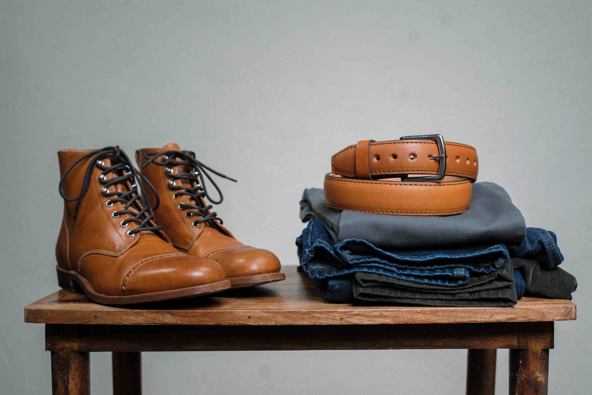 Officer's Boot in English Tan beside a coiled tan leather belt on folded jeans on a wooden stool
