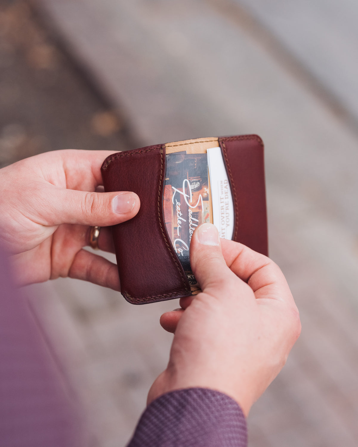 Slim Business Card Holder-Silverback in Oxblood held in both hands as a thumb slides out a business card