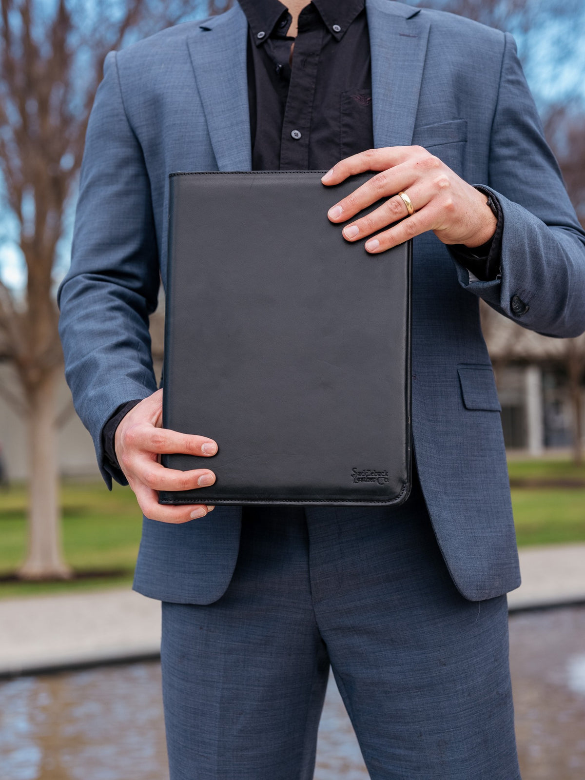 C.S. Lewis Medium Portfolio in Raven Black, closed and held in front by a man in a blue suit outdoors