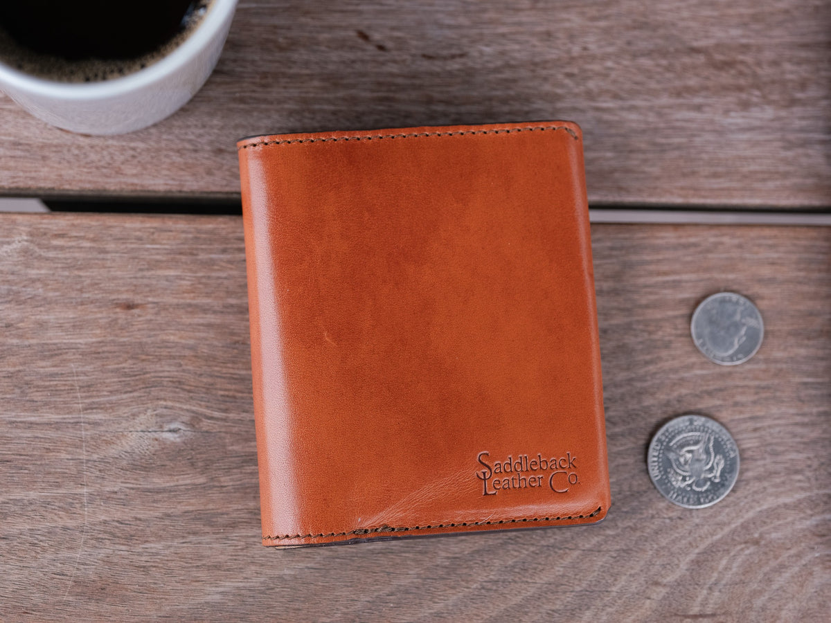 Large Bifold Wallet-Silverback in English Tan, closed front view with debossed logo beside coins and coffee