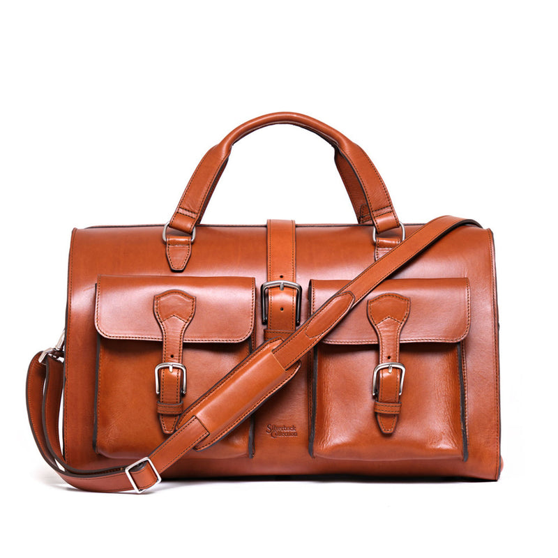 Tan leather duffle bag with two deep buckled front pockets, top handles and a padded shoulder strap.