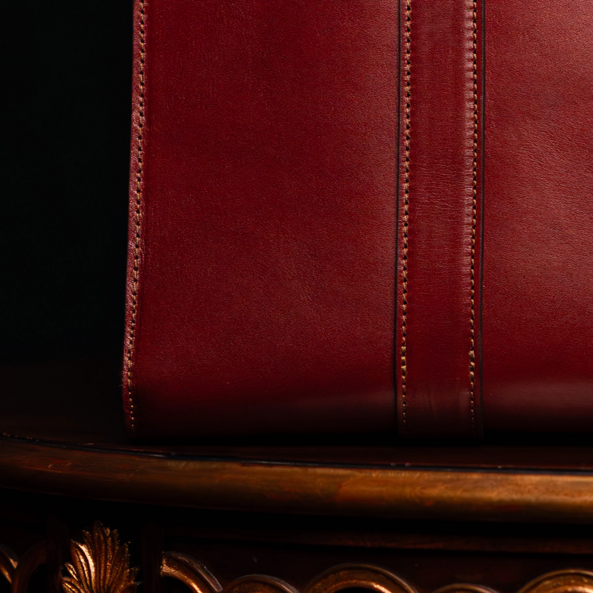 Close-up of the stitching on oxblood leather resting on an ornate gold-toned table