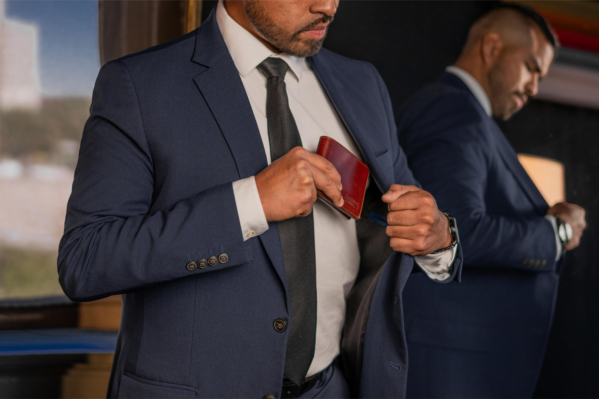 Man in a navy suit sliding an oxblood Silverback William Penn bifold wallet into his inside jacket pocket