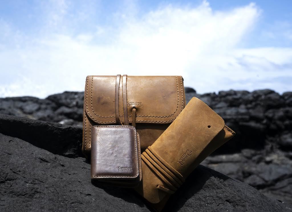 Cash & Receipt Bag in Tobacco on black lava rocks beside other leather goods under a blue sky