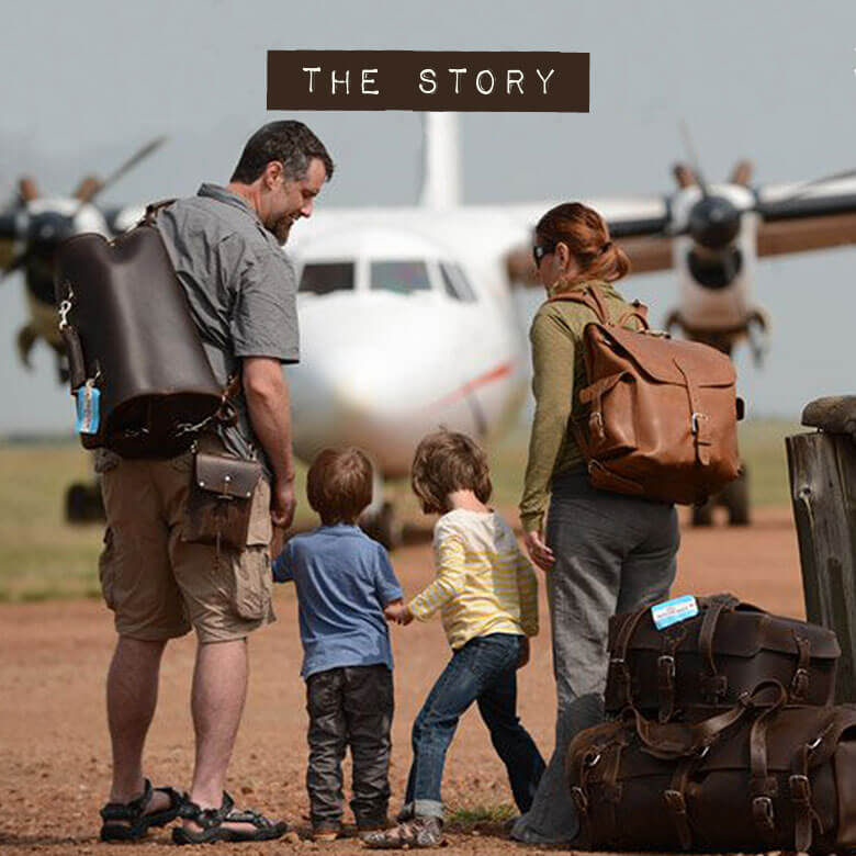 The Story: a father, a mother and two small children, carrying leather bags, walk towards a propeller plane on a dirt airstrip, with more leather luggage stacked beside them.
