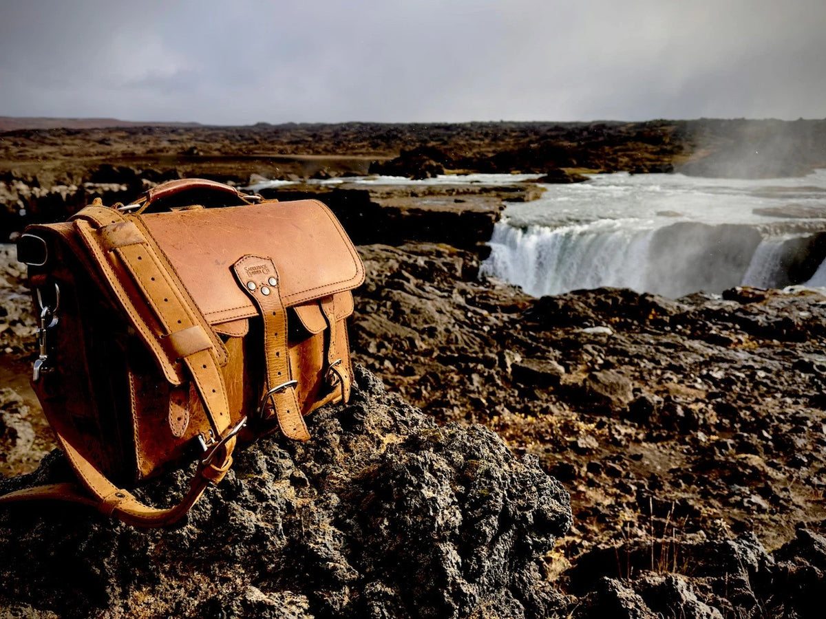 Thin Front Pocket Leather Briefcase in Tobacco on dark volcanic rocks with a wide waterfall behind