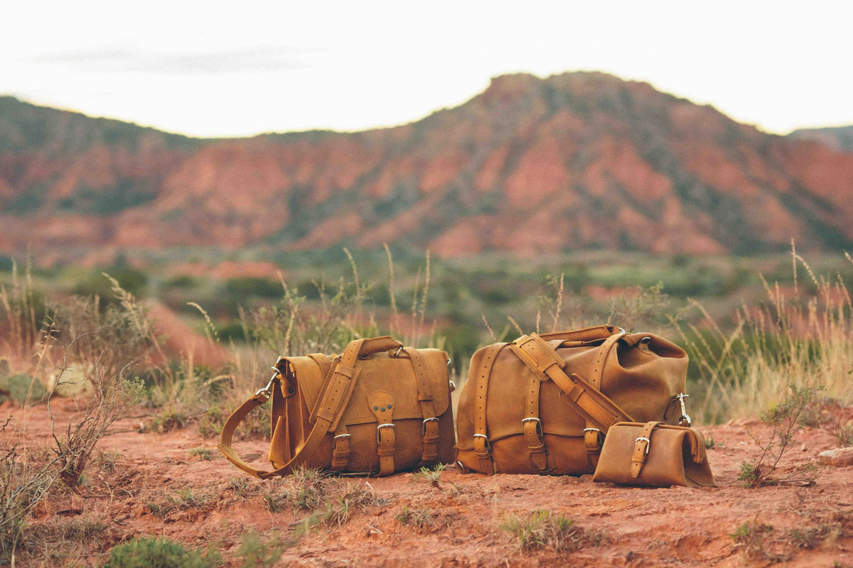 Tobacco leather briefcase, duffle bag and dopp kit together on red dirt at Caprock Canyons