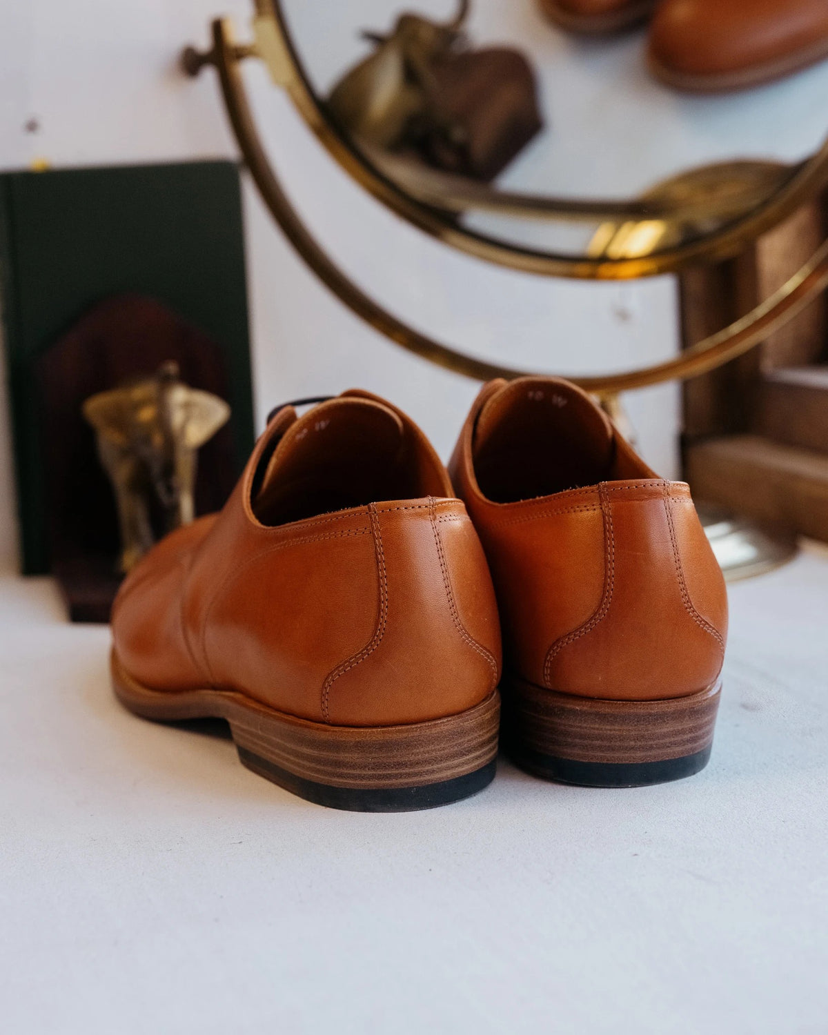 Toe Cap Shoes - English Tan, back view of a pair showing the stacked leather heels beside a brass mirror