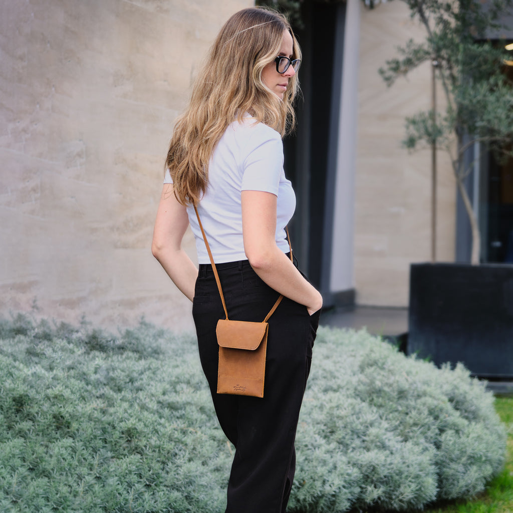 Walker's Pouch in tan, worn crossbody by a woman in a white tee and black pants outdoors