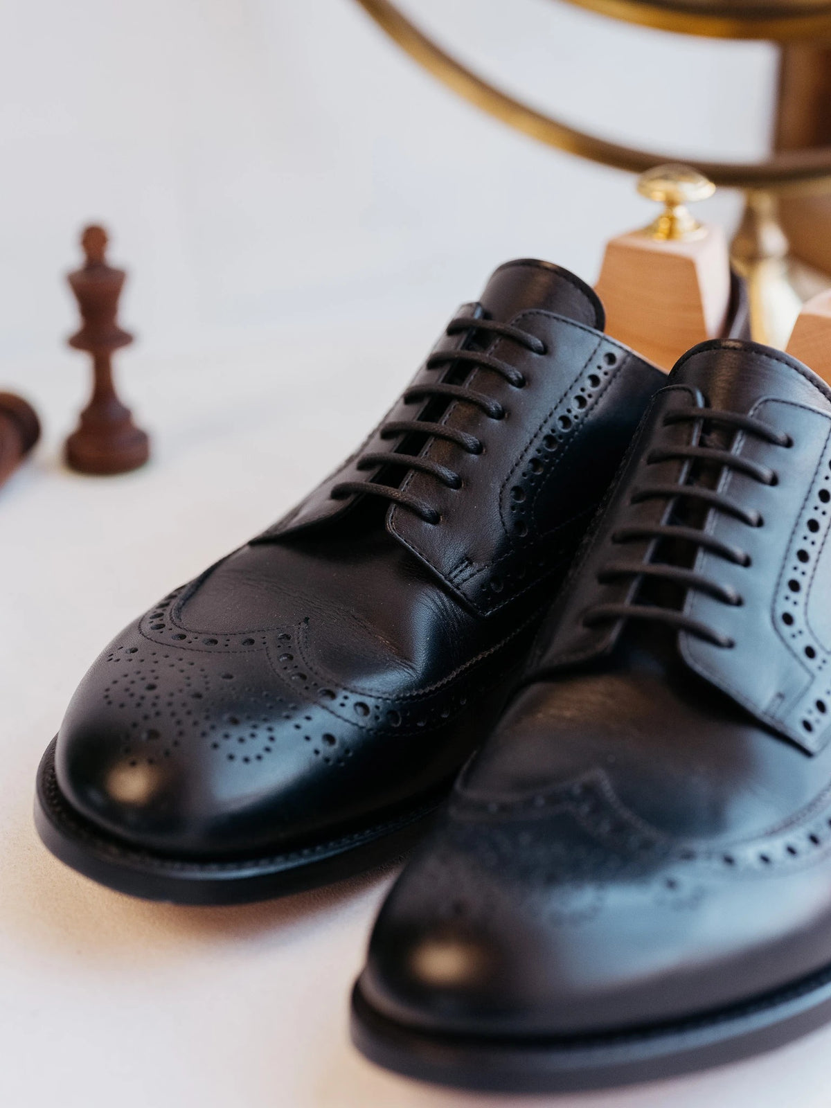 Wingtip Shoes - Raven Black, close-up of the brogued toes of a pair beside a wooden chess piece