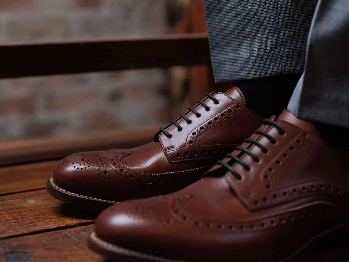 Wingtip Shoes - Chestnut on foot, close side view of a pair with grey trousers on a wooden floor