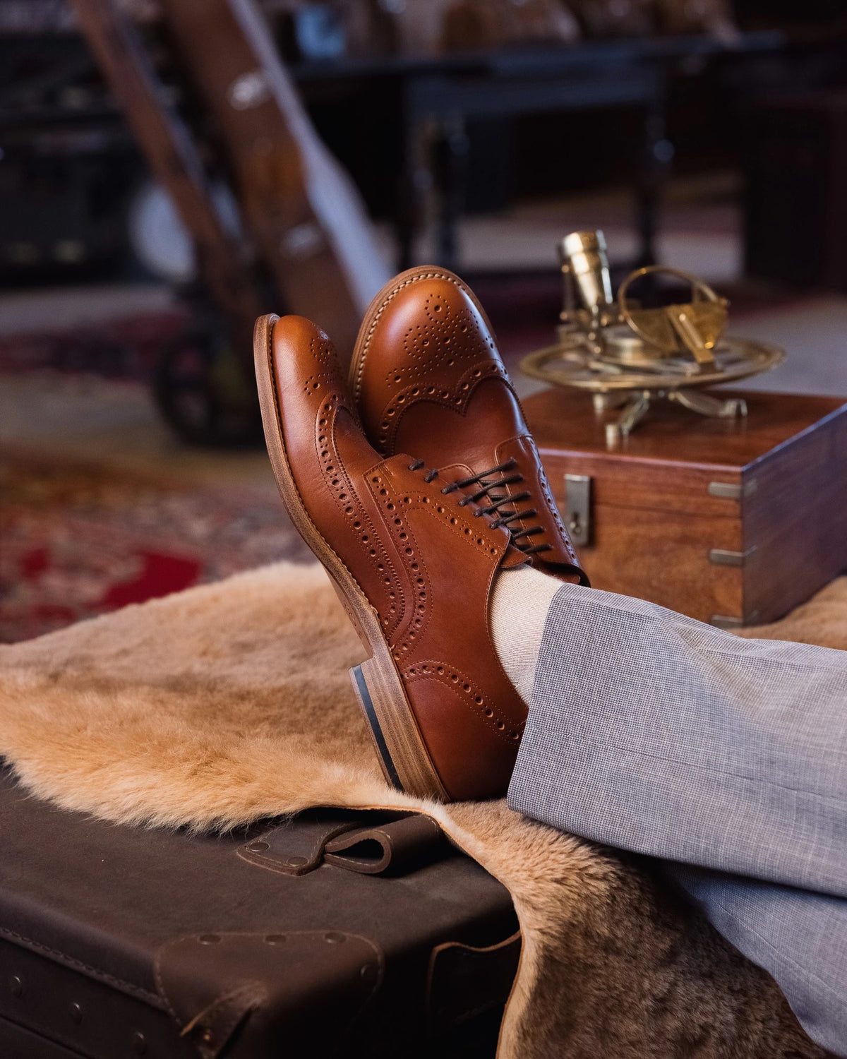 Wingtip Shoes - Natural Tan, side view of crossed feet up on a sheepskin-covered trunk by a wooden box and sextant
