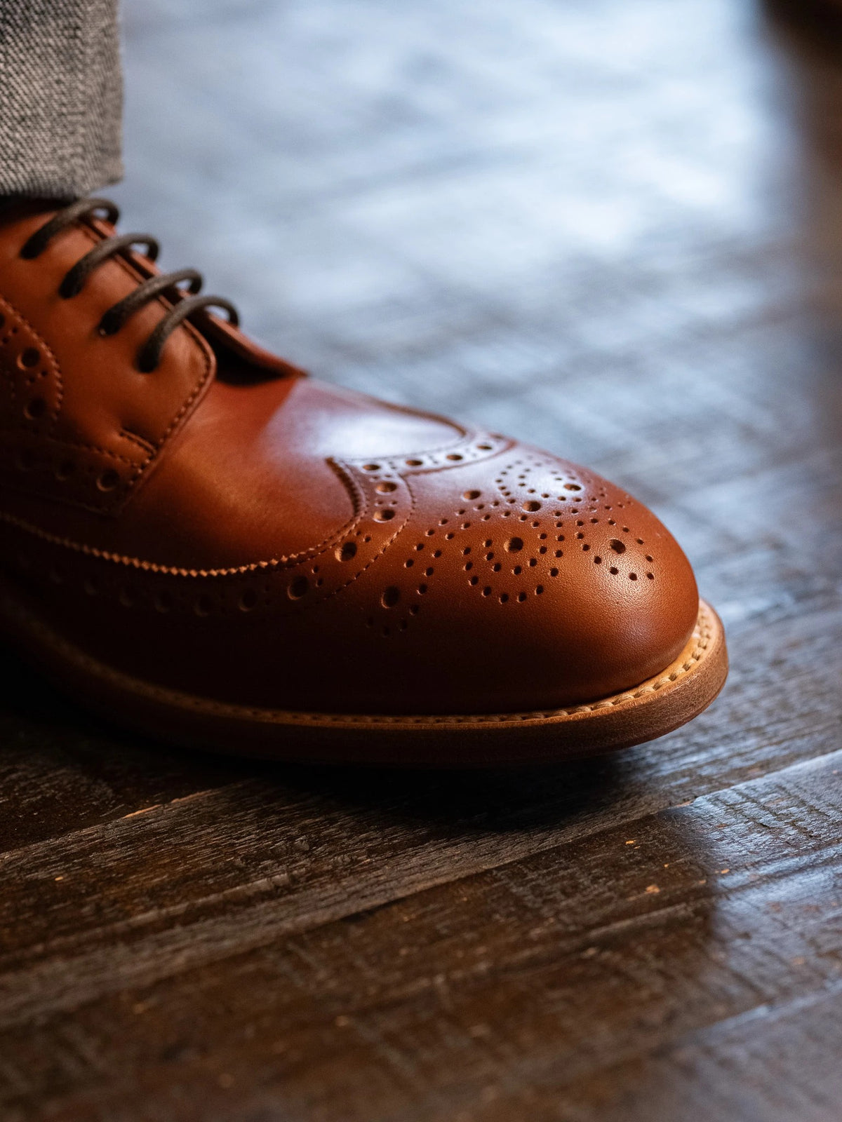 Wingtip Shoes - Natural Tan, close-up of the brogued wingtip toe and welt on a wood floor